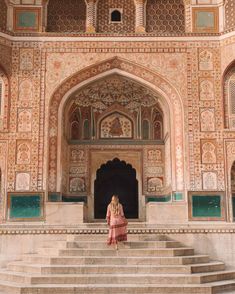 a woman standing on steps in front of a building with intricately decorated walls and doorways