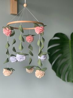 a pink and purple flower mobile hanging from a wall next to a green leafy plant