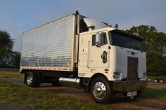 a white semi truck parked on top of a grass covered field with trees in the background