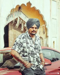 a man in a turban standing next to a red car with his hands on his hips