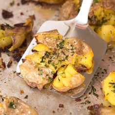 a pan filled with cooked potatoes covered in seasoning next to a spatula on top of it