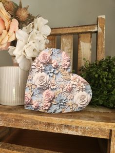 a heart shaped box sitting on top of a wooden table next to a vase with flowers