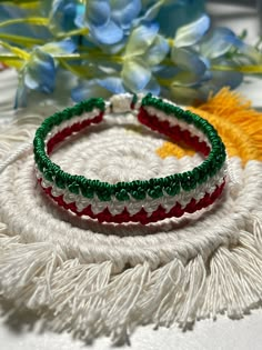 two bracelets with green, red and white beads on a table next to flowers