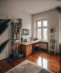 a room with a desk, chair and bookshelf next to a large window