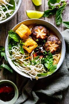 a bowl filled with noodles, tofu and vegetables next to some dipping sauces