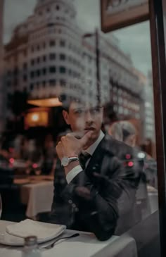 a man sitting at a table in front of a window with his hand on his chin