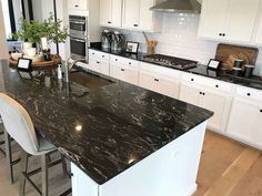 a kitchen with white cabinets and black marble counter tops, along with an island in the middle