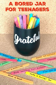 a black cup filled with colored pencils sitting on top of a table next to writing utensils