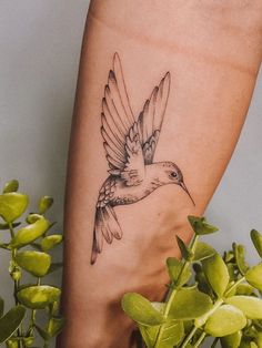 a small bird tattoo on the foot of a woman's right leg, next to some green plants