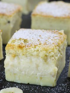 several pieces of cake with powdered sugar on top and bananas around the edges, sitting on a black surface