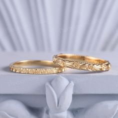 two gold wedding rings sitting on top of a white box with a flower design in the middle