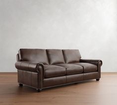 a brown leather couch sitting on top of a wooden floor next to a white wall