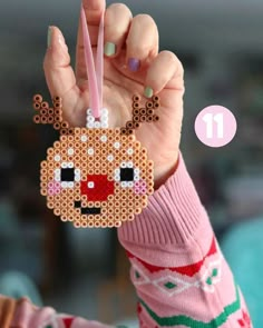 a person holding up a beaded ornament with a reindeer face on it