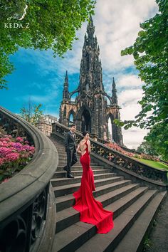 a woman in a red dress is standing on some steps near a man in a black suit