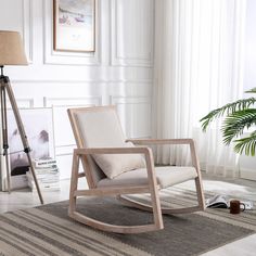 a white rocking chair sitting on top of a rug in a living room next to a lamp