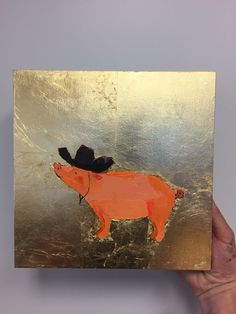 a hand holding up a piece of art with a pig on it's back