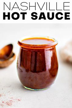 a glass jar filled with hot sauce on top of a white counter next to a spoon