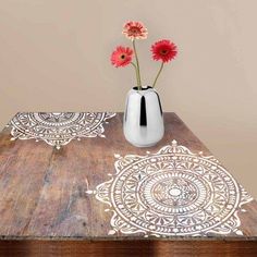 a wooden table topped with a white vase filled with flowers next to a red flower