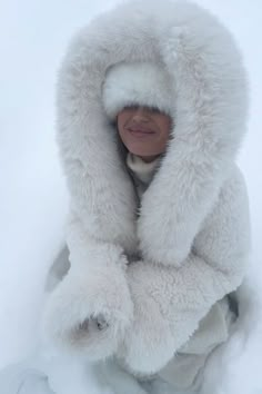 a woman wearing a white fur coat in the snow with her arms wrapped around her head