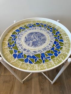 a blue and green plate sitting on top of a white table next to a wooden floor