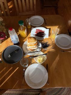 a wooden table topped with white plates and dishes covered in cake next to bottles of orange juice