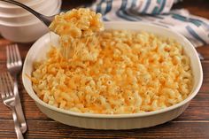 a spoon full of macaroni and cheese being lifted from a dish with a fork