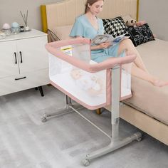 a woman sitting on a bed reading a book next to a baby in a crib