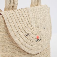 a straw bag with an orange flower on the front and two eyes drawn on it