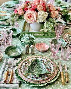 the table is set with plates, silverware and pink flowers in a green vase