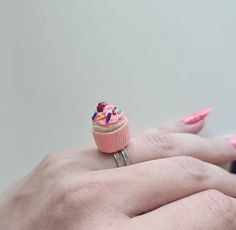 a woman's hand holding a pink ring with a cupcake on it and sprinkles