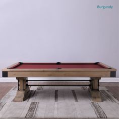 a pool table in the middle of a room with a rug on the floor and a white wall behind it