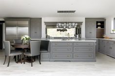 a large kitchen with gray cabinets and marble counter tops, along with a dining room table surrounded by grey chairs