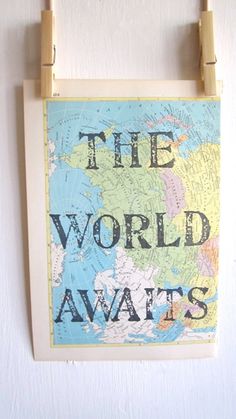 the world awaits poster hanging on a wall with clothes pegs in front of it