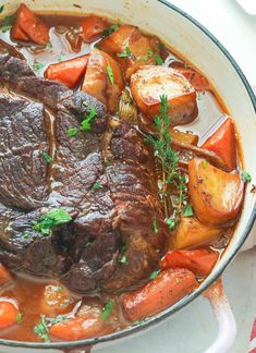 pot roast with carrots, potatoes and parsley in a white bowl on a table