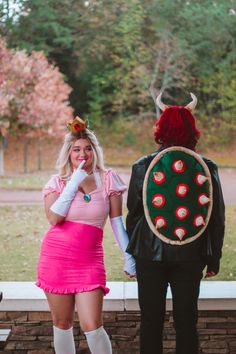 two people dressed in costumes standing next to each other near a brick wall and trees