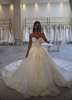 a woman in a wedding dress taking a selfie with her cell phone at the bridal gown shop