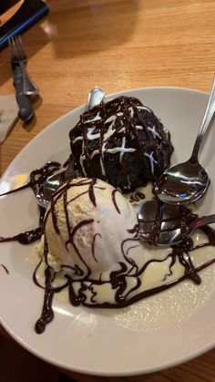 an ice cream sundae on a white plate with chocolate drizzle and spoons