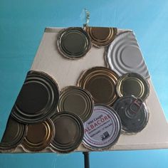 a lamp shade made out of tin cans on a blue tablecloth with buttons attached to it