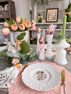 the table is set for easter dinner with pink flowers in vases and bunny figurines