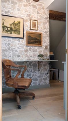 an office chair sitting in front of a stone wall with pictures on the wall above it