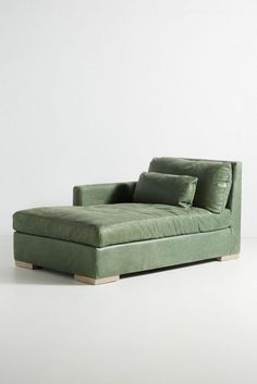 a green chaise lounge chair with pillows on the back and arms, in front of a white wall