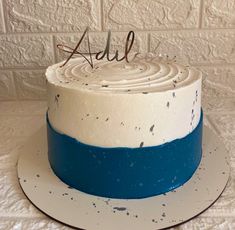 a white and blue cake with the word add on it sitting on a plate next to a brick wall