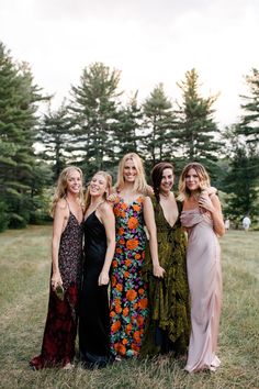 four women in dresses posing for the camera with trees in the backgroung