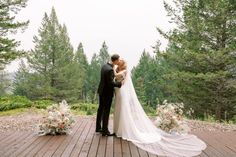 a bride and groom kissing on a deck surrounded by trees