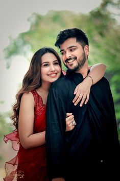 a man and woman hugging each other in the middle of an outdoor photo shoot with trees in the background