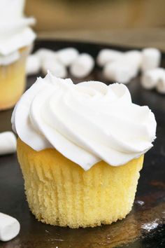 a cupcake with white frosting sitting on top of a black plate