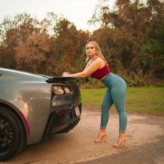 a woman leaning on the hood of a sports car with her hands in the trunk