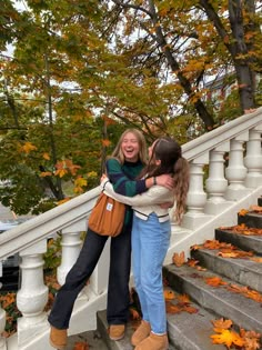 two girls hugging each other on the steps in front of some trees with fall leaves