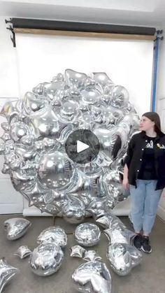 a woman standing in front of a bunch of silver balloons that look like an object