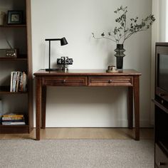 a wooden table with a vase on it next to a book shelf